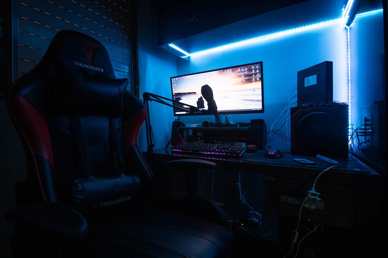 A sleek gaming desk with a monitor, gaming chair, and LED lights creating an immersive environment.